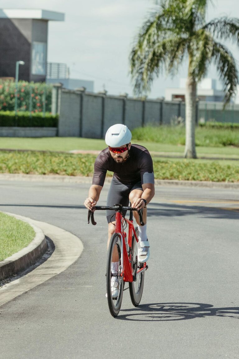 A male cyclist in sport attire biking on a city street under bright sunlight for exercise.