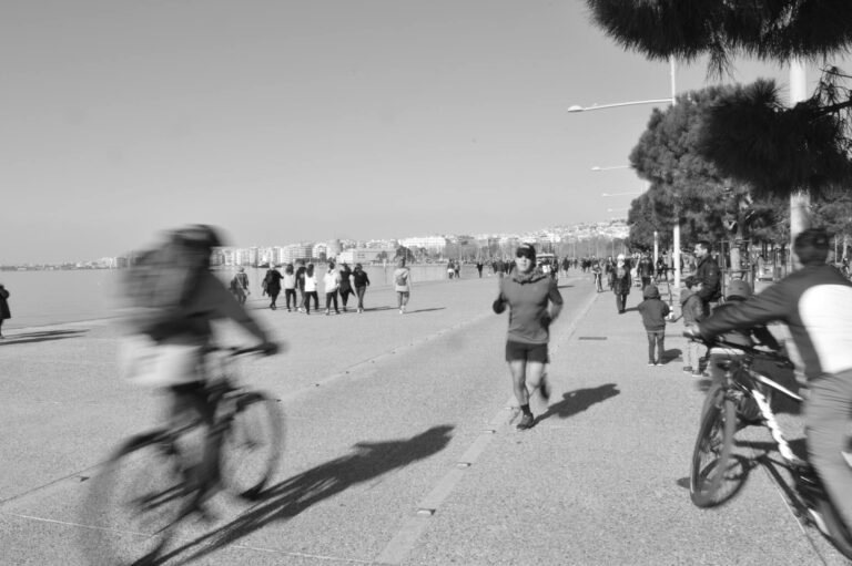 Black and white photo of a busy seaside promenade with cyclists and runners.